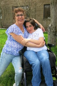 A female Liberty ARC staff embraces a young woman in a wheelchair supported by Liberty.