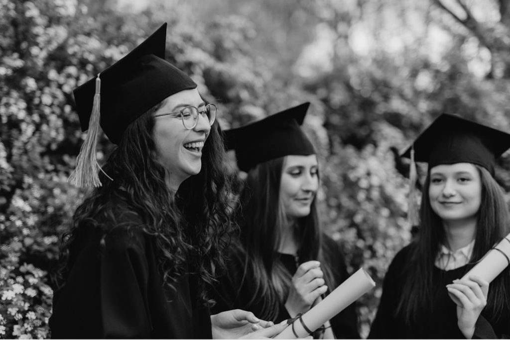 Three women smiling in their cap and gowns for gradation holding their diplomas.